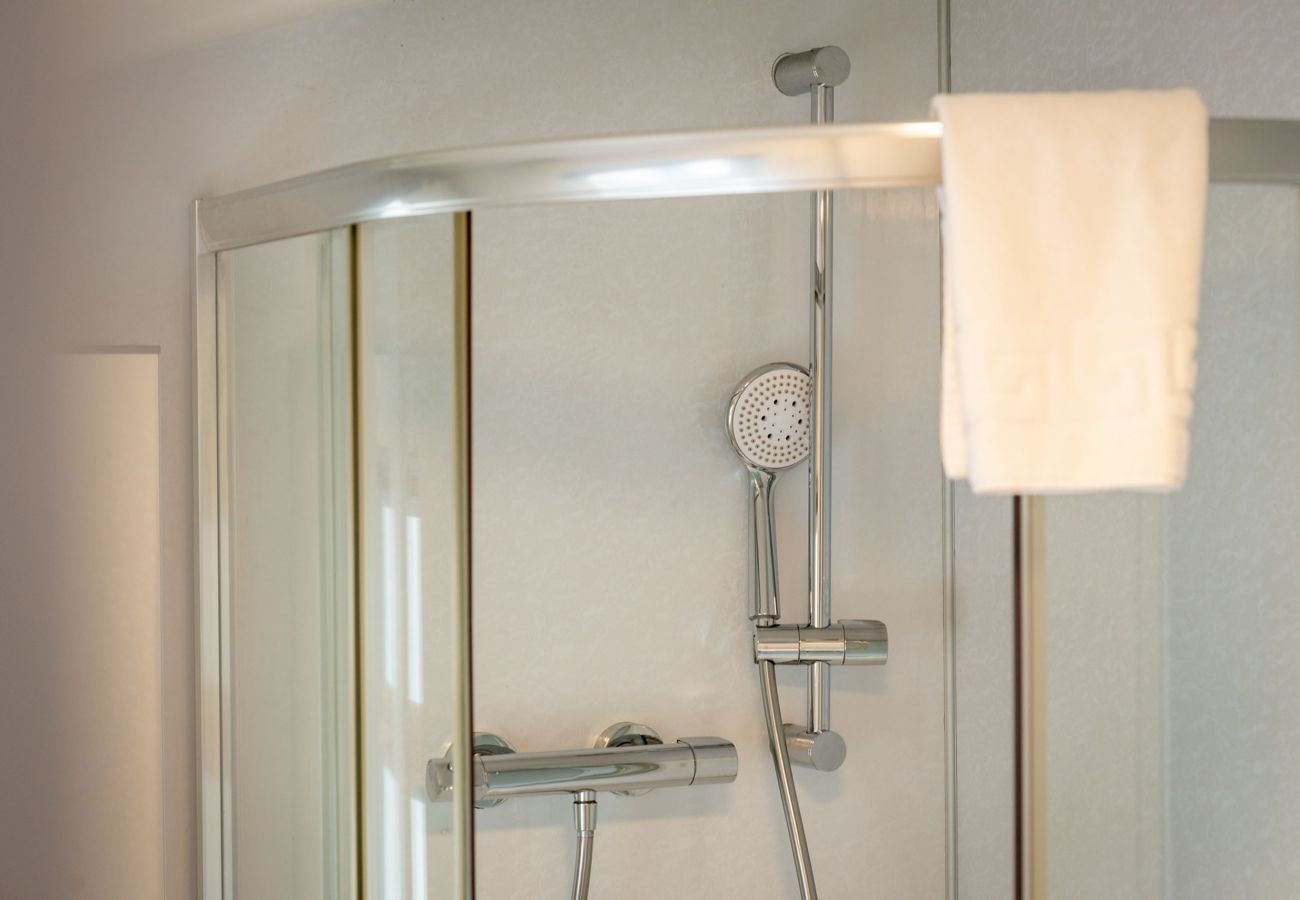 Close-up of curved shower door with chrome shower and hanging towel.