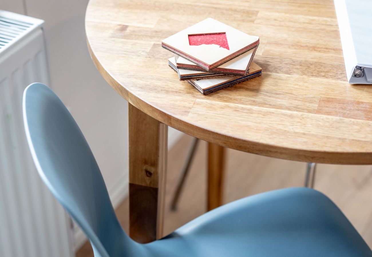 Round wooden table with a blue chair and stacked coasters on top.