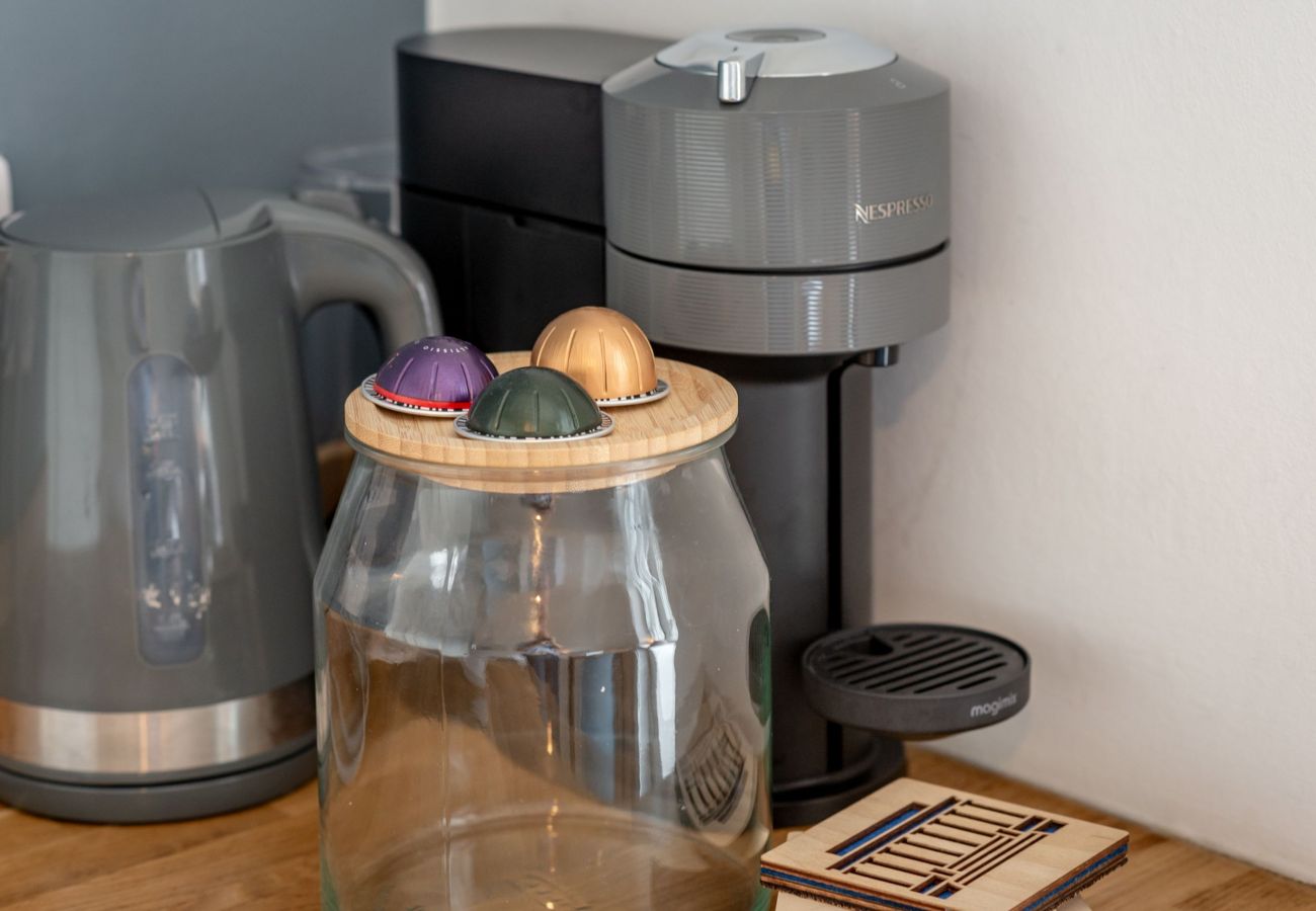 Coffee machine, kettle, and jar with colourful pods on wooden counter.