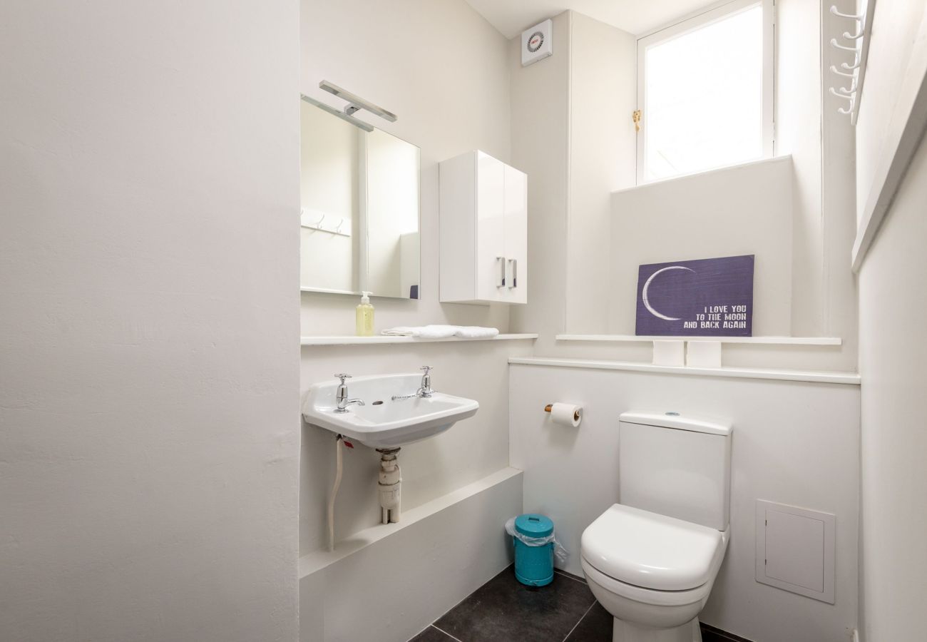 Neatly presented guest toilet with white walls, a wall-mounted sink, mirrored cabinet, and frosted window.