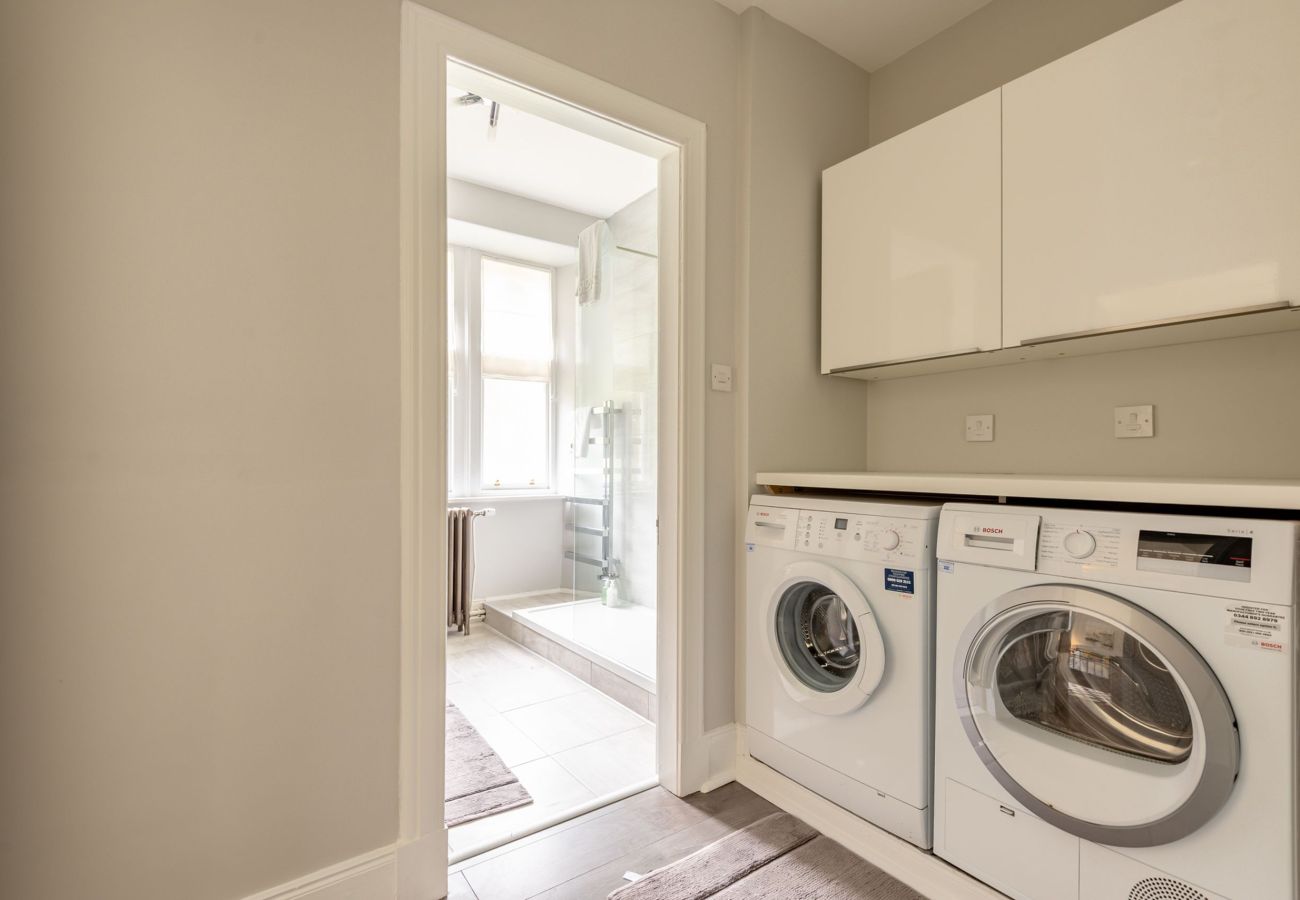 Practical laundry area with Bosch washing machine and dryer, overhead storage, and view into the bathroom beyond.