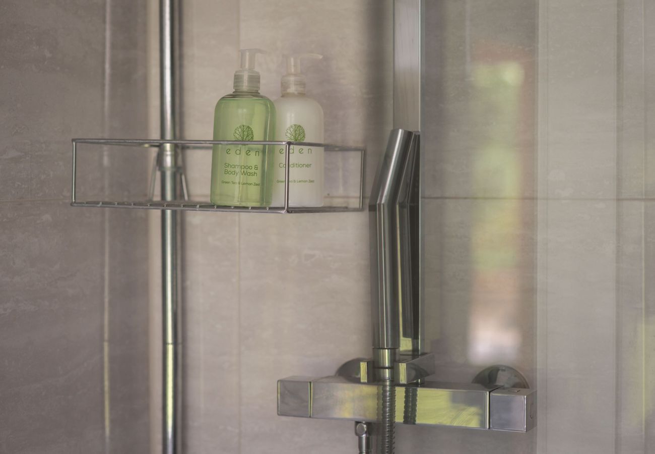 Contemporary tiled shower with chrome fittings and a shelf holding Eden shampoo and conditioner