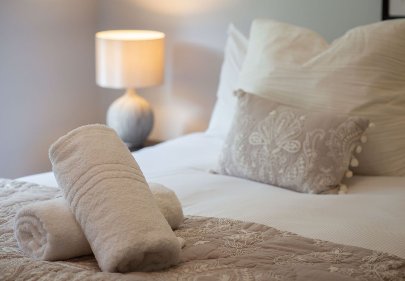 Bedroom with soft beige bedding, decorative pillows, and fresh towels arranged on the bed