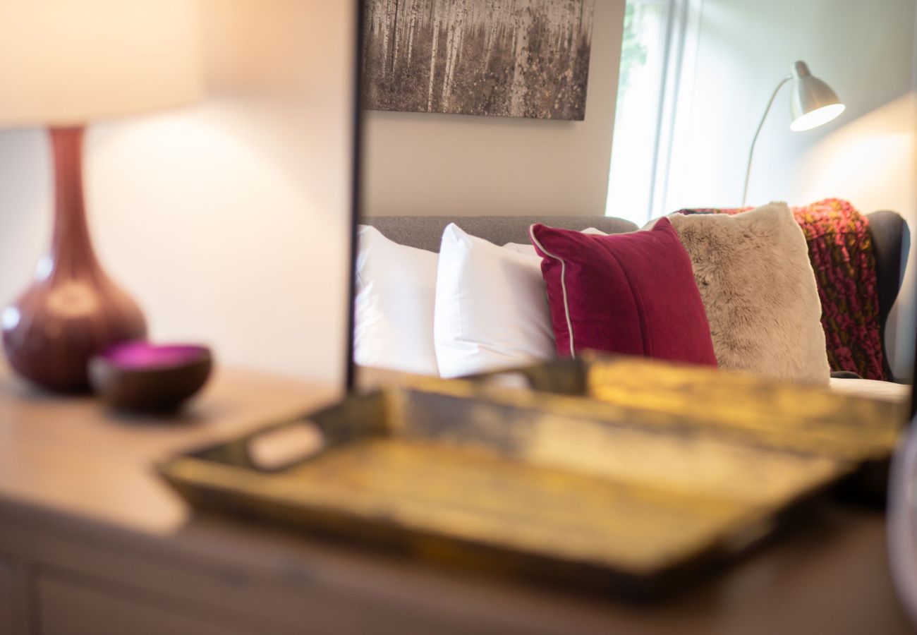 Mirror reflection showing a well-made bed with deep red cushions and a warm lamp glow