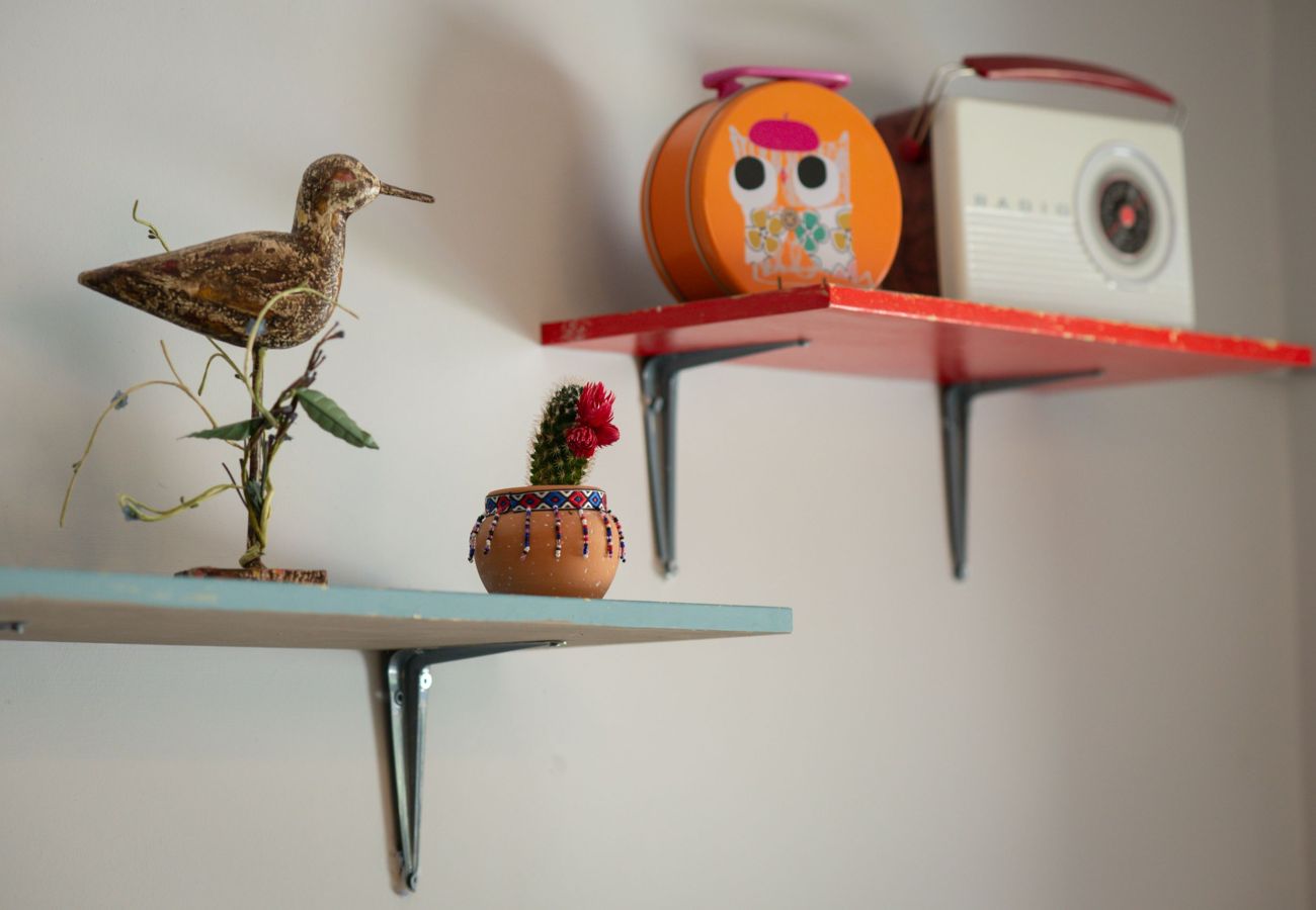 Colourful shelves featuring a wooden bird, a cactus in a beaded pot, and vintage ornaments