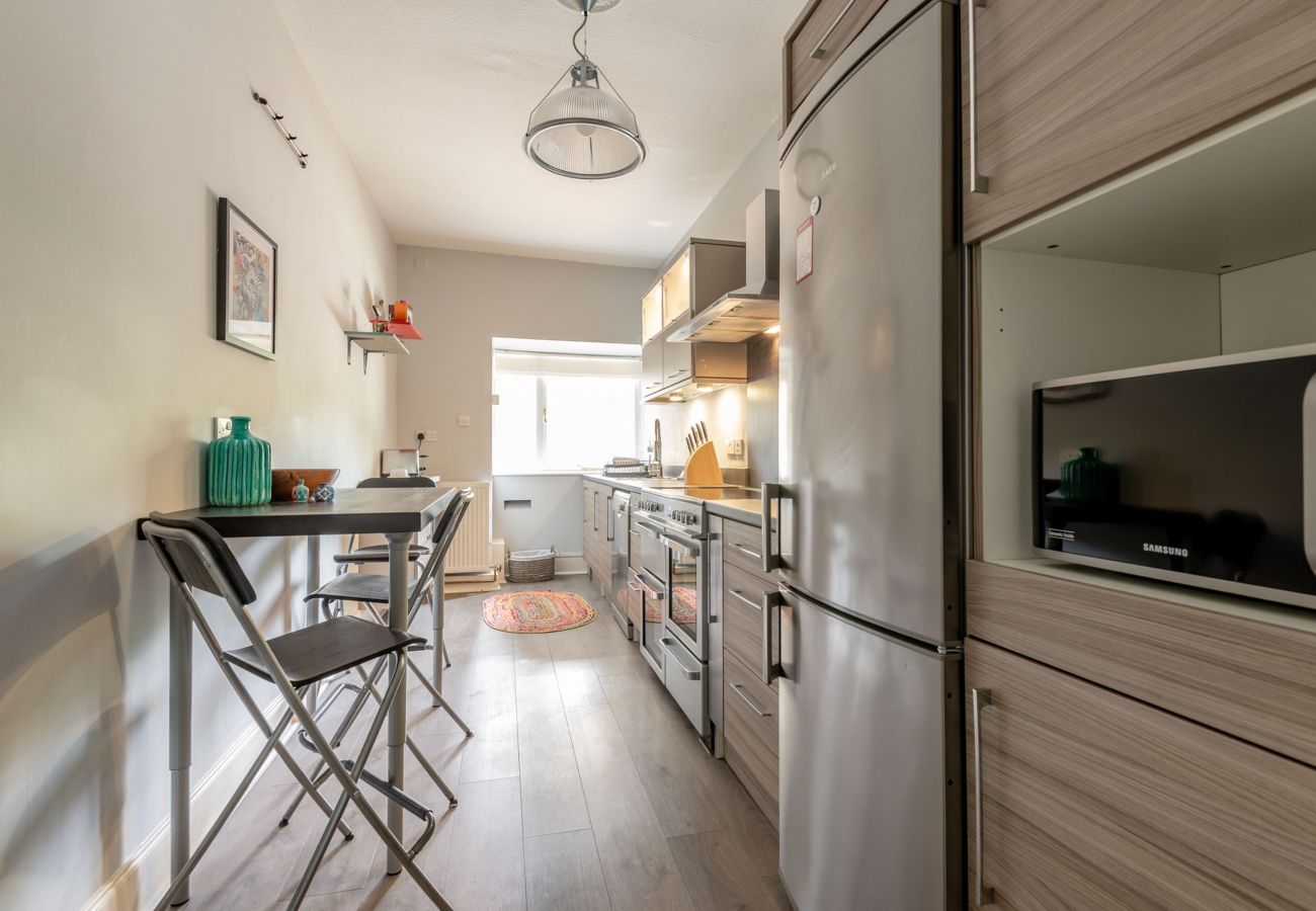 Modern galley-style kitchen featuring wood cabinets, stainless steel appliances, breakfast bar with high stools, and window at the far end.