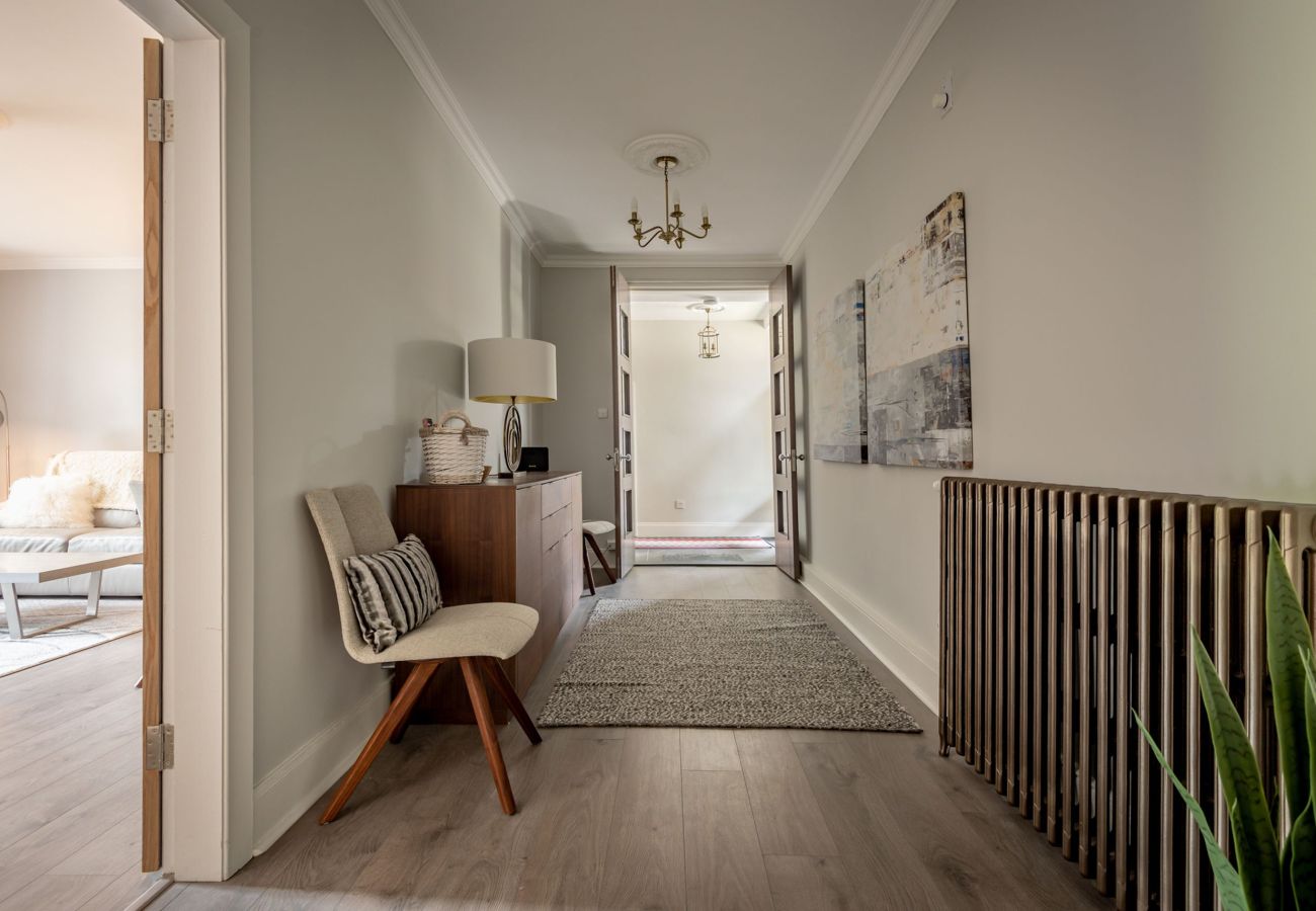 Wide hallway with decorative chandelier, wooden sideboard, soft grey tones, and artwork on the wall.