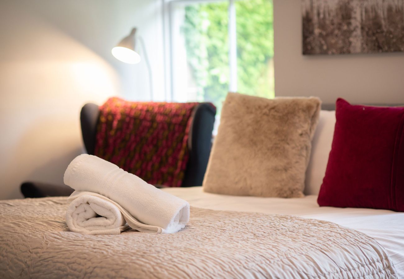 Bed with plush cushions and throw, bedside lamp, and a window overlooking greenery