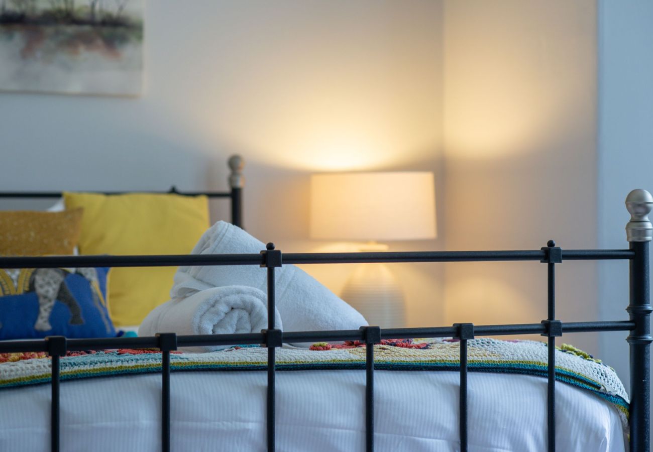 Neatly made bed with vibrant cushions, rolled white towels, and a softly lit table lamp