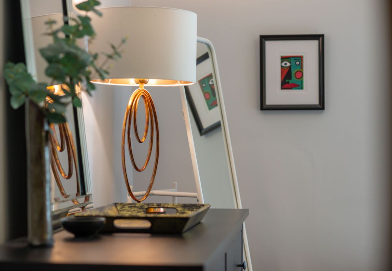 Close-up of a bedroom dresser with decorative tray, gold looped lamp, and a colourful framed print