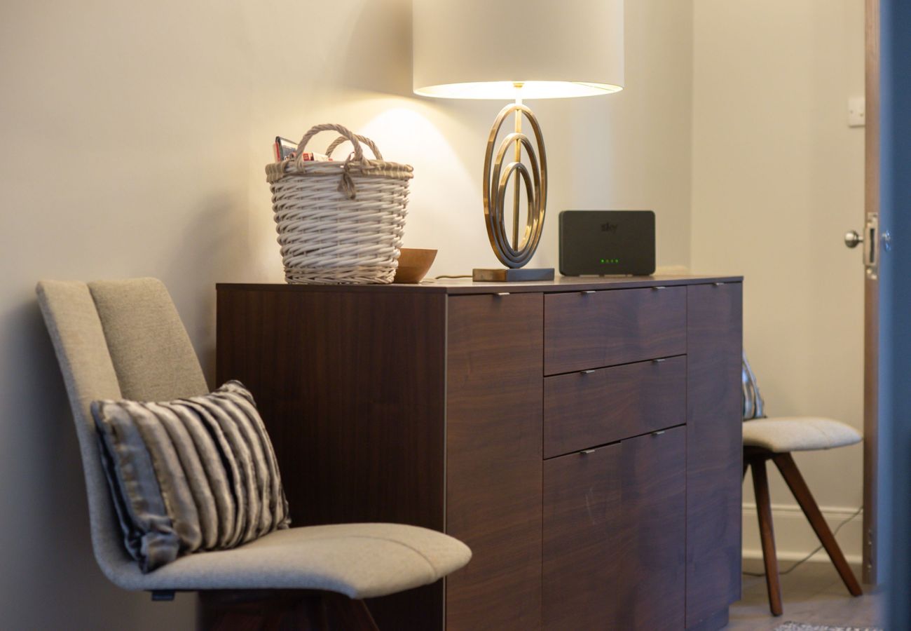 stylish bedroom detail featuring a wooden sideboard, sculptural lamp, woven basket, and cushioned chairs.