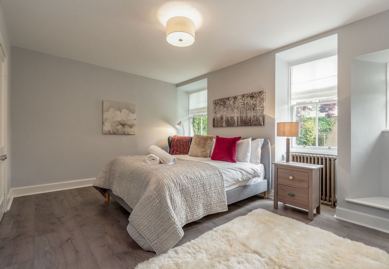 Light-filled bedroom with textured bedding, stylish decor, and two tall windows offering a garden view.