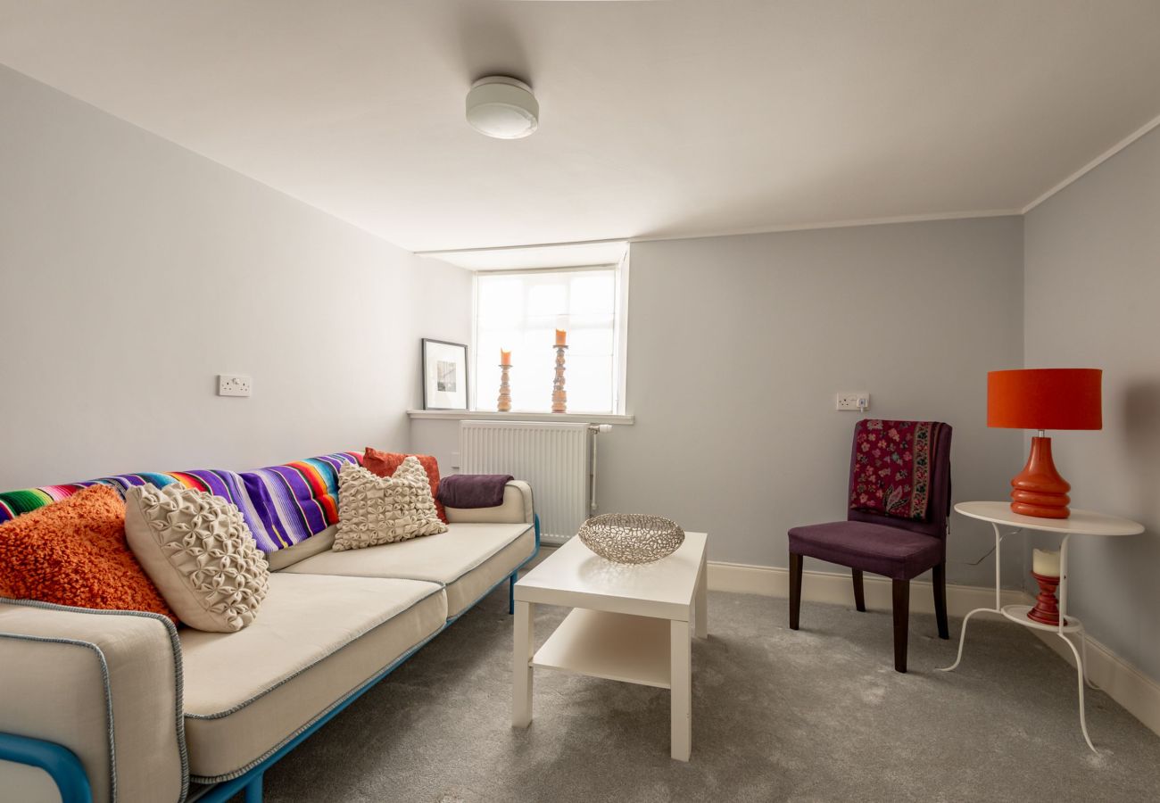 Compact living room with a bright throw-covered sofa, eclectic cushions, and vibrant lighting creating a relaxed, playful vibe.