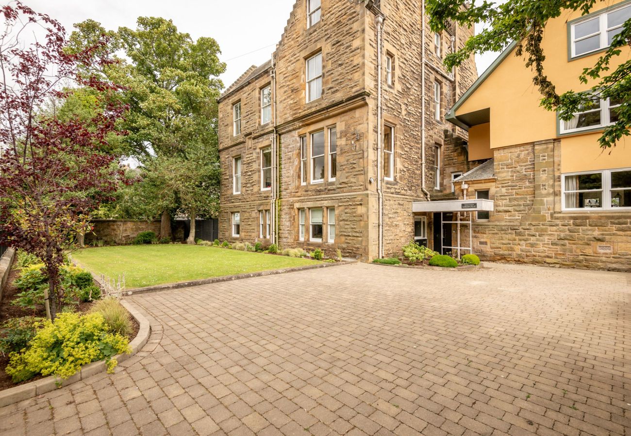 Period stone building with large sash windows, cobbled drive, and neatly edged grass lawn in a leafy residential setting.