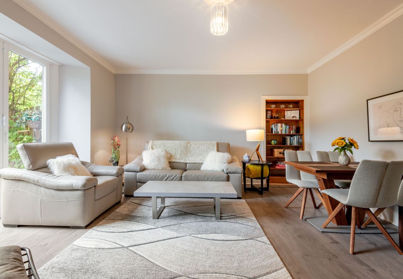 Contemporary living and dining room featuring neutral armchairs, modern bookcase, dining table, and minimalist décor.
