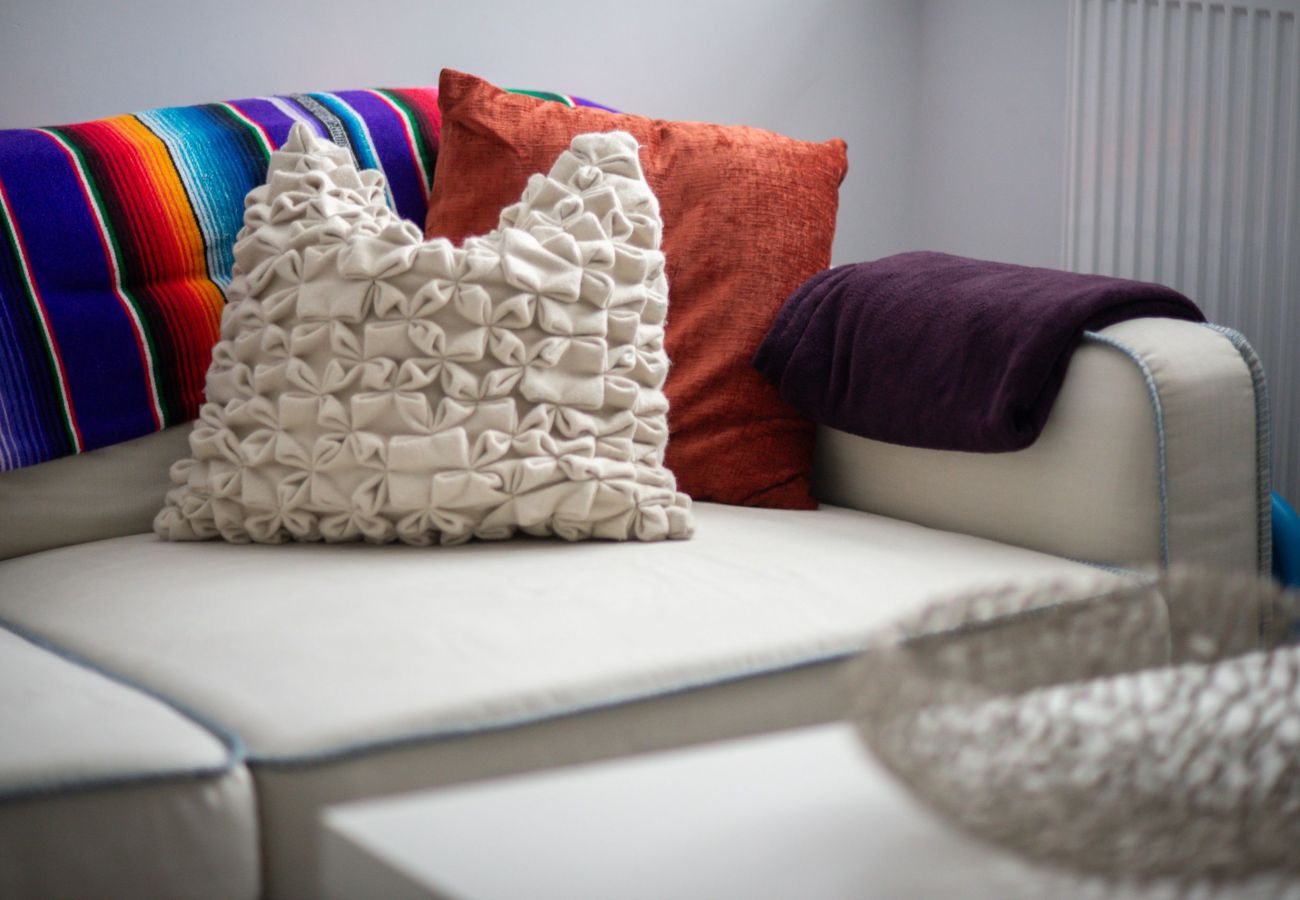 Neutral-toned corner sofa with a ruched cushion, bright Mexican-style throw, and coloured pillows