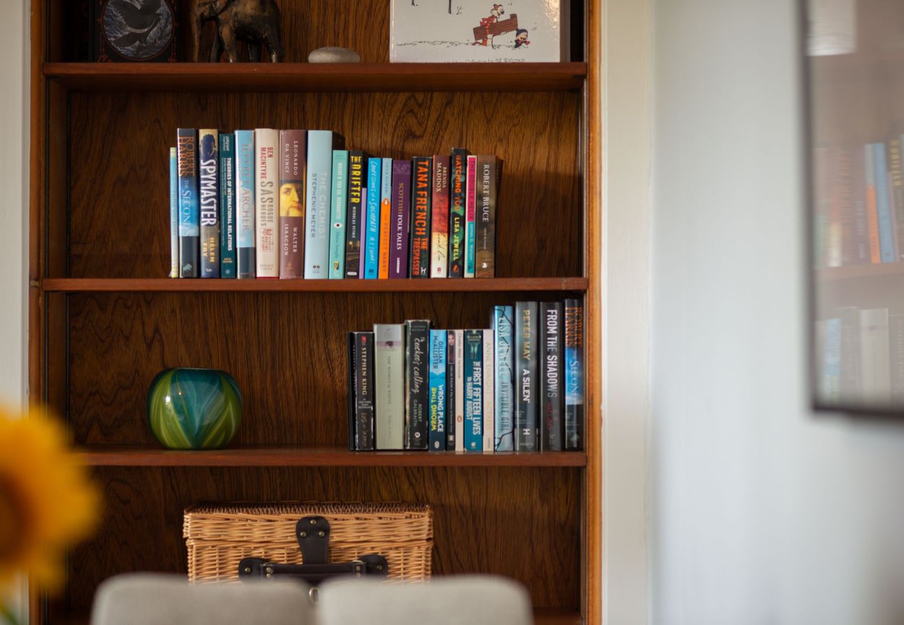 Warm wood shelves filled with colourful books, wicker basket, glass vase, and decorative animal figures.