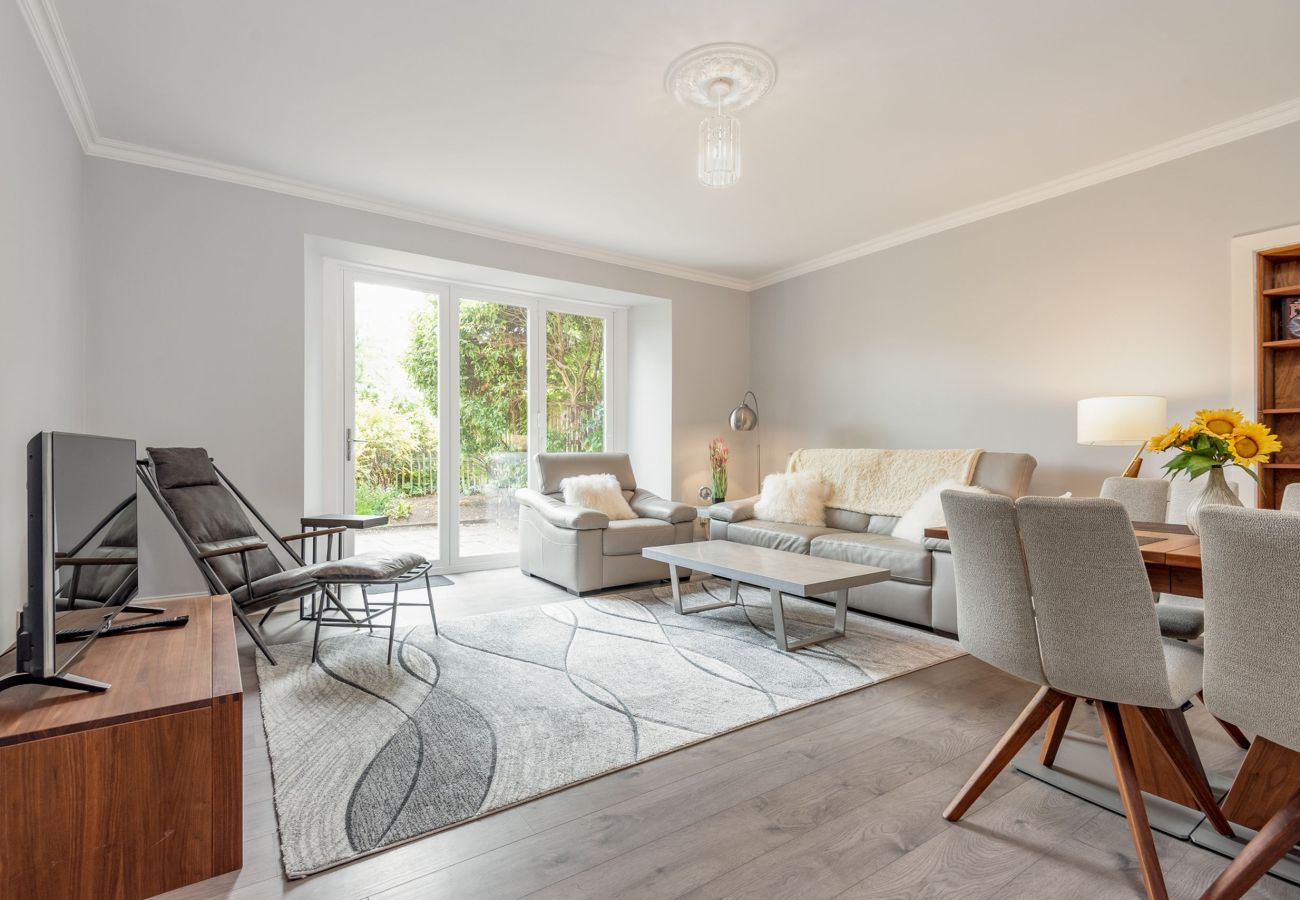 Open-plan lounge and dining space with large bi-fold doors to the garden, soft neutral seating, and wooden dining table.