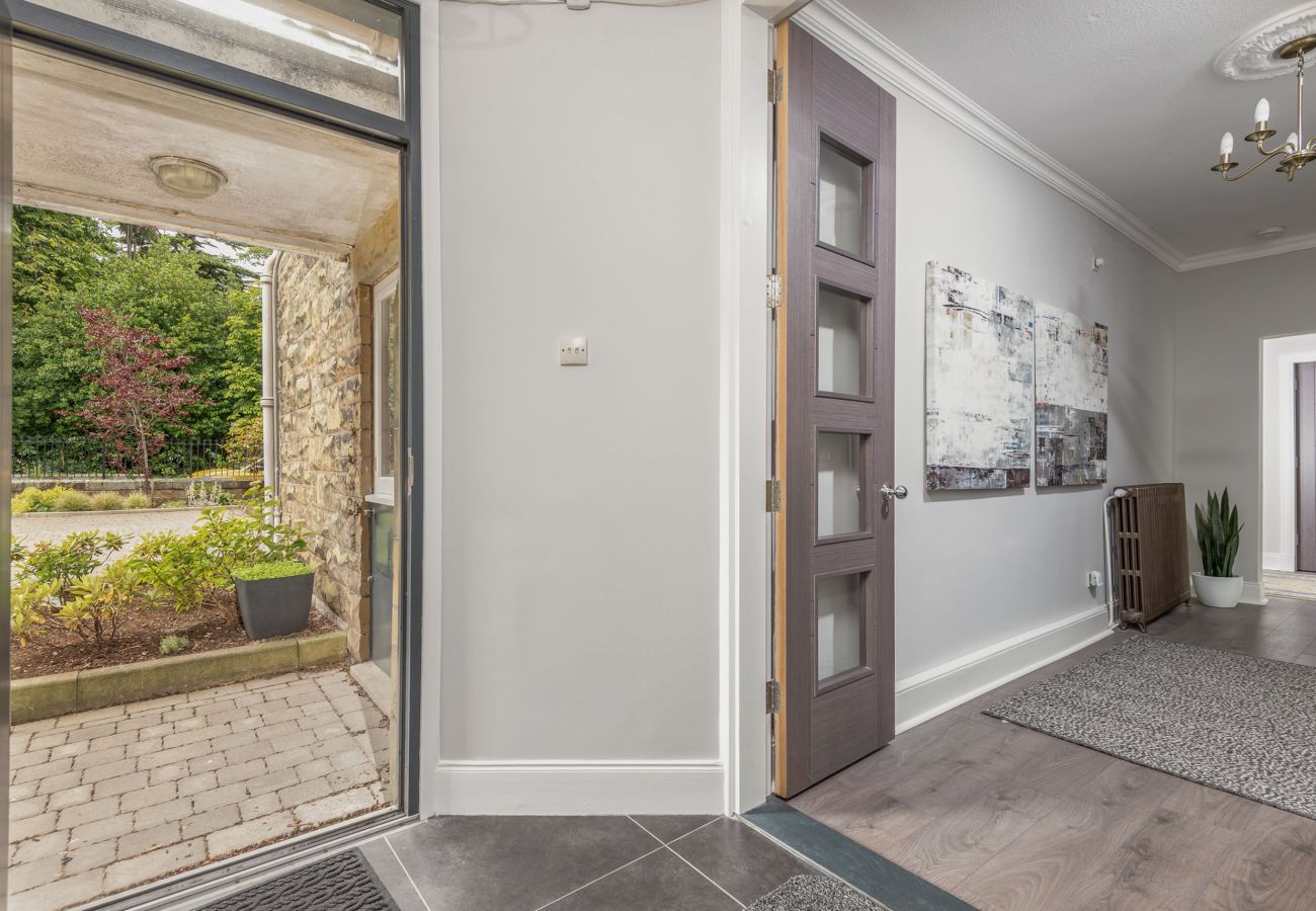 Modern hallway with wooden flooring, contemporary doors, and view of landscaped front garden through open glass door.