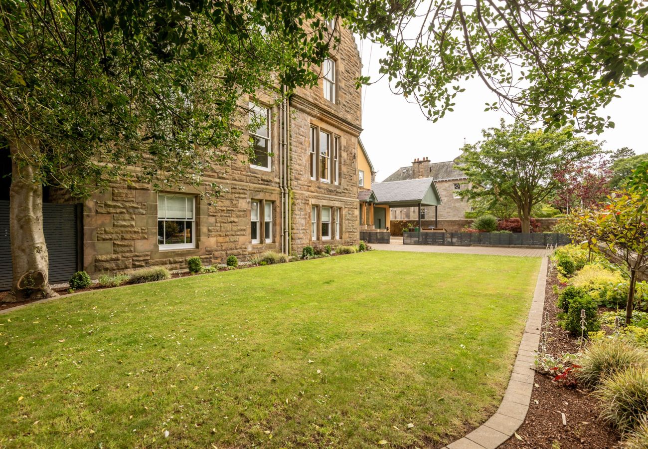 Open green space with trimmed lawn, mature shrubs, and garden edging wrapping around a handsome sandstone building.