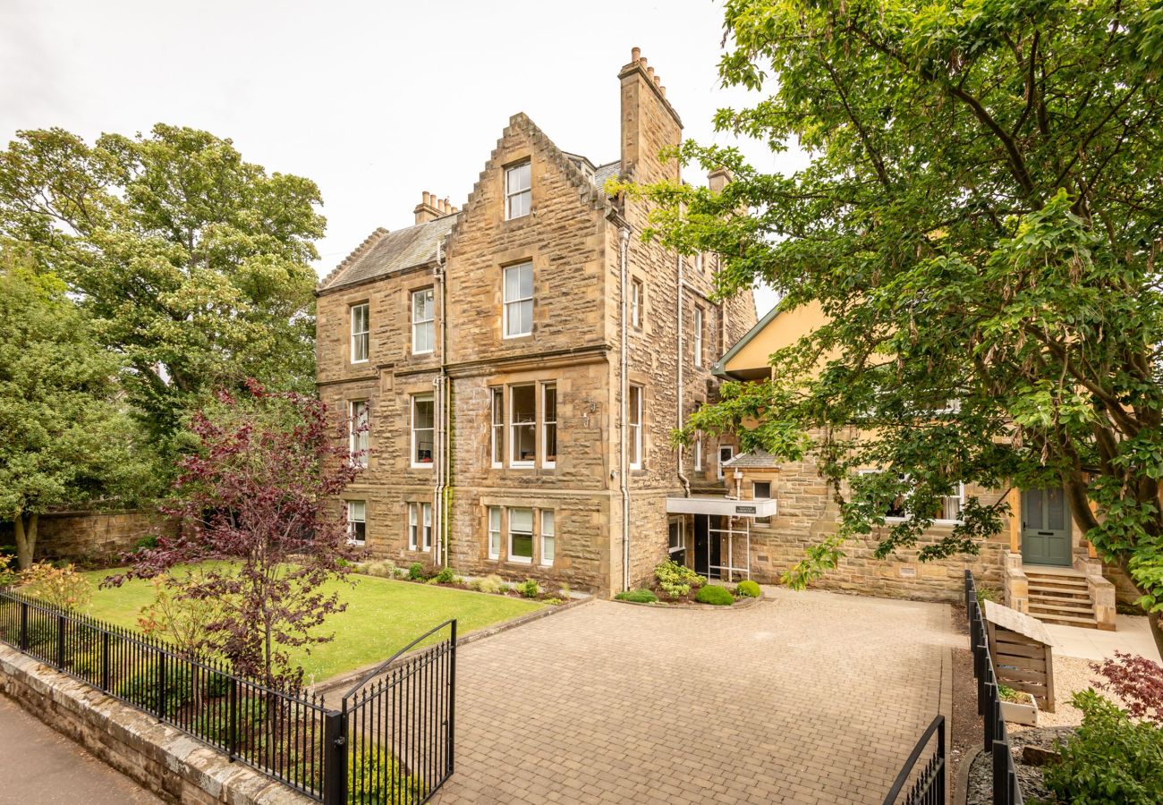 Impressive Victorian stone residence with gabled roof and gated entrance, set within landscaped grounds.