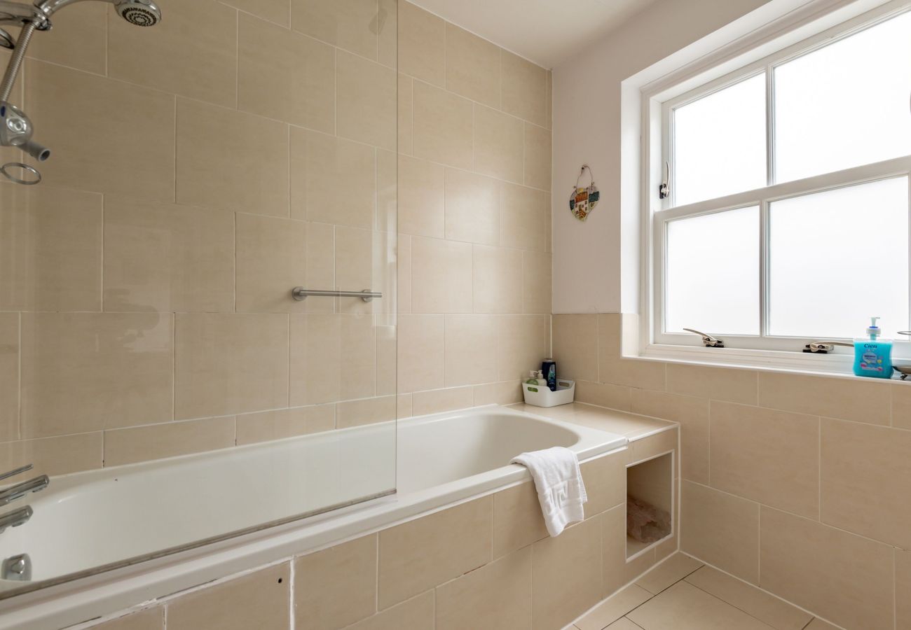Neutral-tiled bathroom with shower over bath and frosted window at Earls Lodge, Earlsferry.