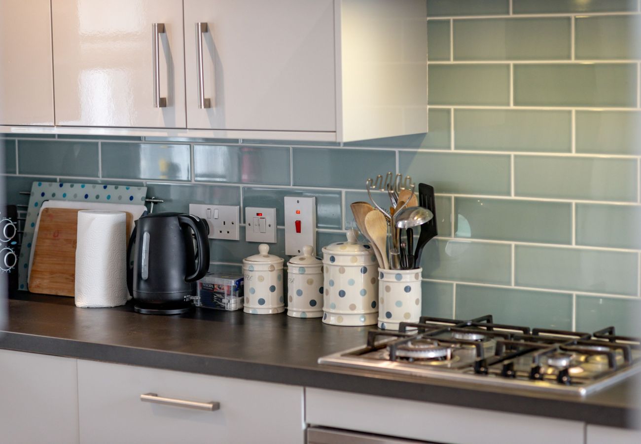 Sleek kitchen with gas hob, glossy cabinets and green subway tiles at Earls Lodge holiday home.