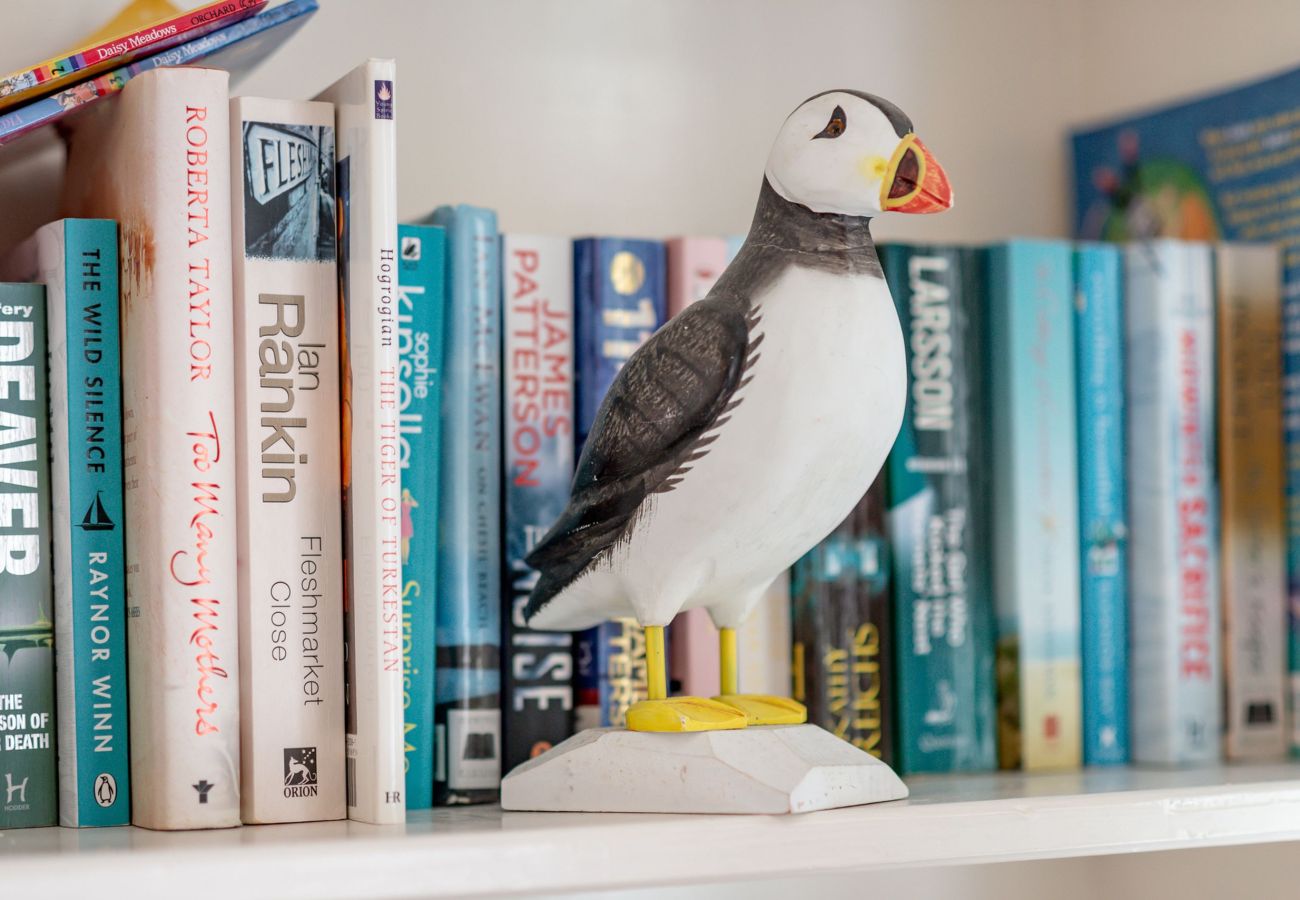 Bookshelf with coastal titles and puffin ornament in the lounge at Earls Lodge, Earlsferry.