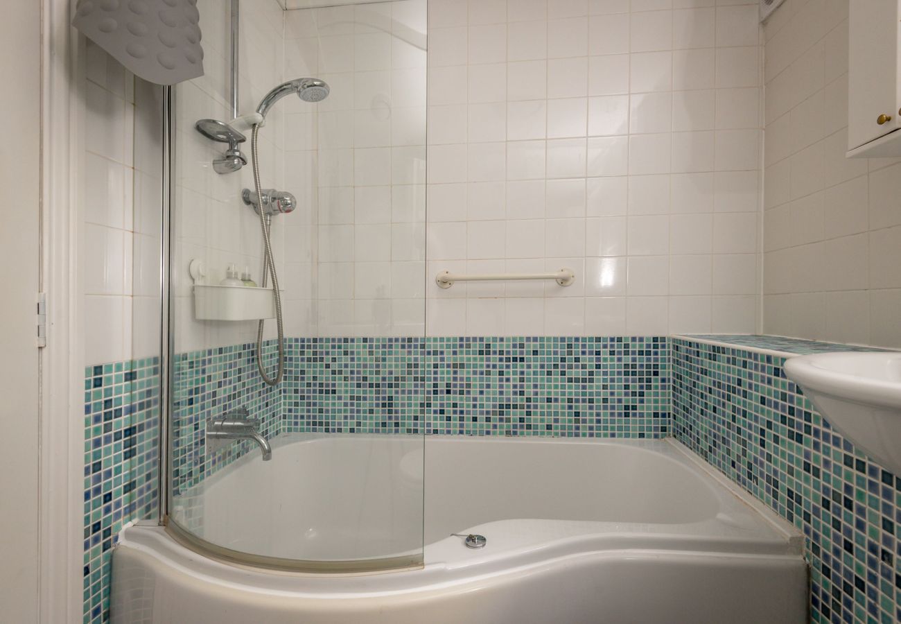 White tiled bathroom with P-shaped bathtub, overhead shower and blue mosaic tiling in St Andrews rental.