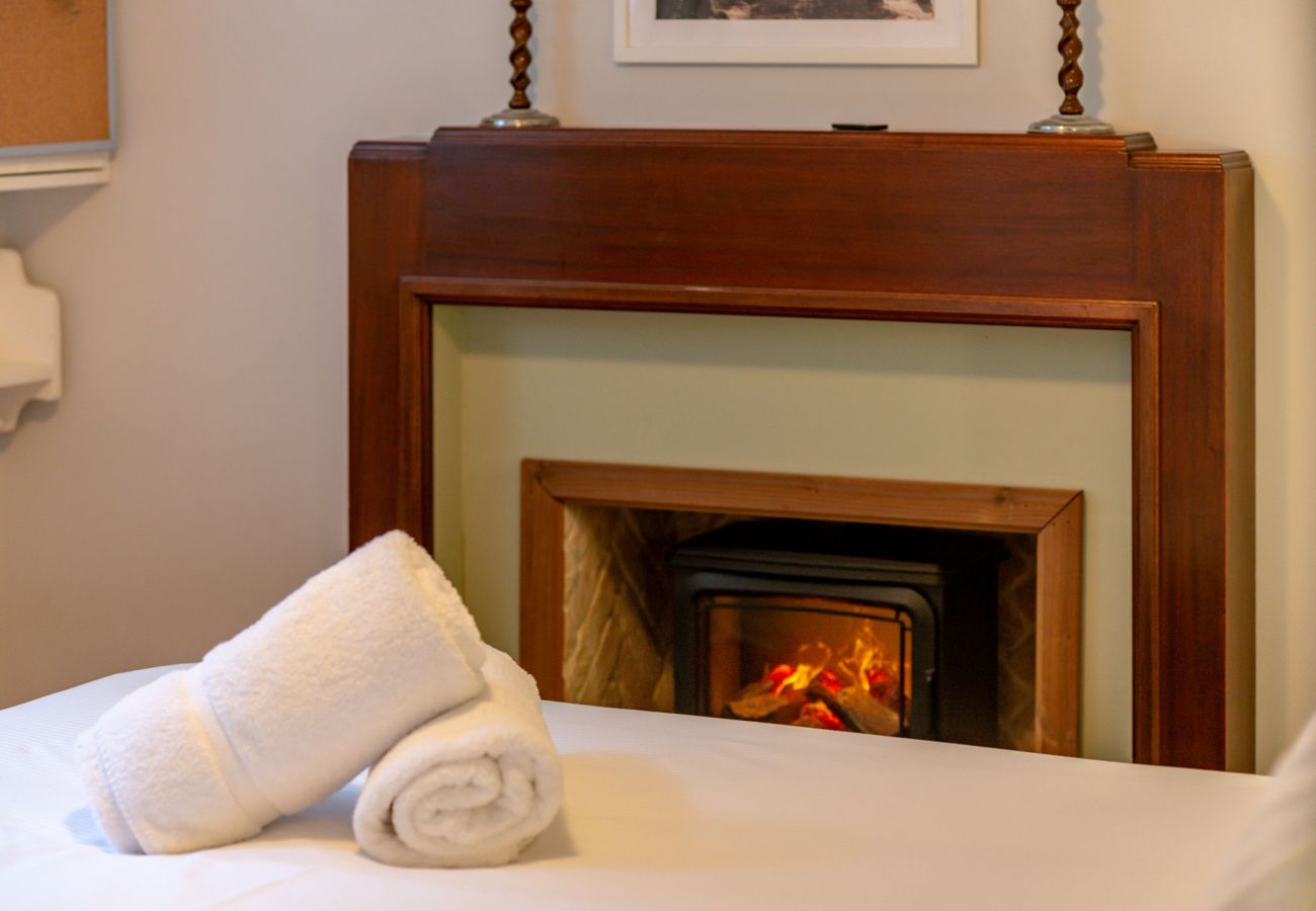 Fresh towels on bed facing cosy electric stove in wooden-surround fireplace at 42 Lade Braes, St Andrews.