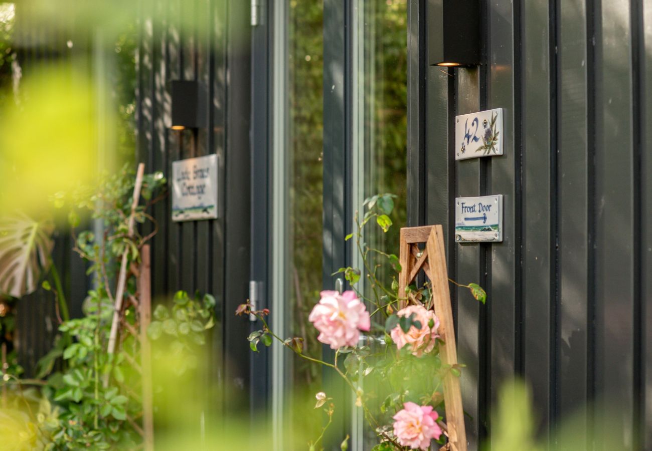 Exterior with roses, directional signs and 42 plaque by glass door at 42 Lade Braes self-catering, St Andrews.